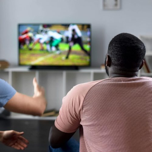 Male friends gather to watch football competition on big screen, sofa experts